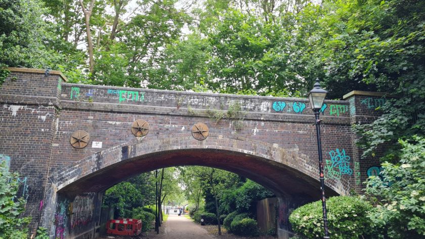 Looking through a dark brown brick railway bridge, trees line either side of the image.
