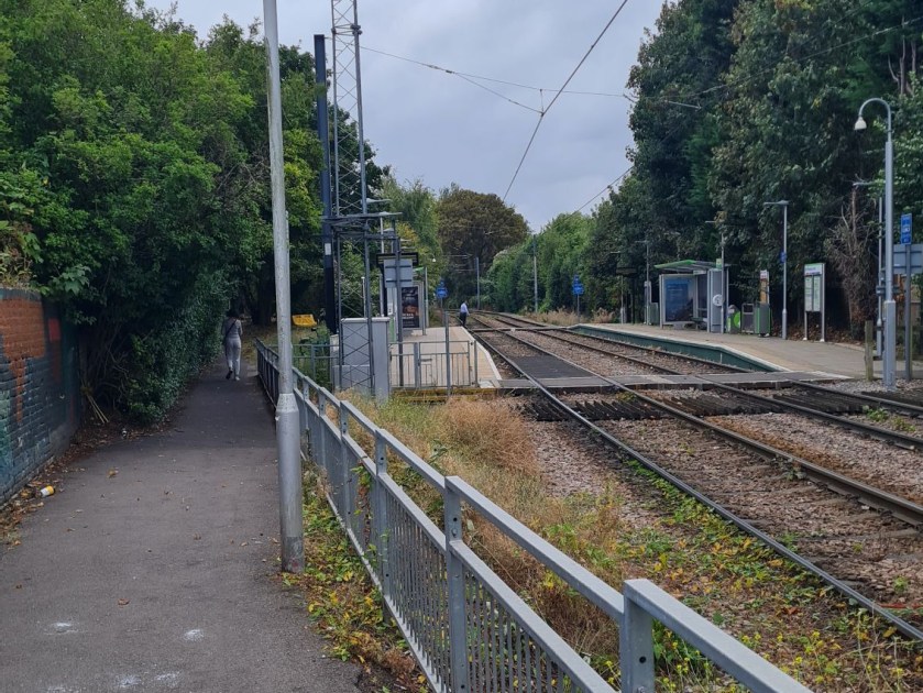 Merton Park tram stop is in the background on the right. It has two tracks. To the left is a footpath which follows the path of the Merton loop. The divergence of the two old lines can be seen in this picture.