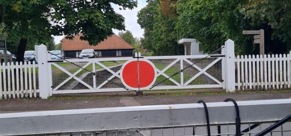 Across the road from the remains of Bramley & Wonersh station. On either side of the road are replica old white and red manual level crossing gates.
