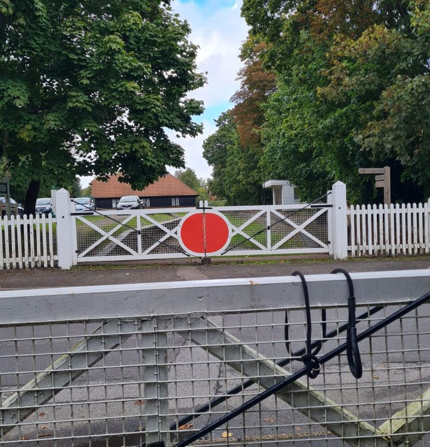 Across the road from the remains of Bramley & Wonersh station. On either side of the road are replica old white and red manual level crossing gates.